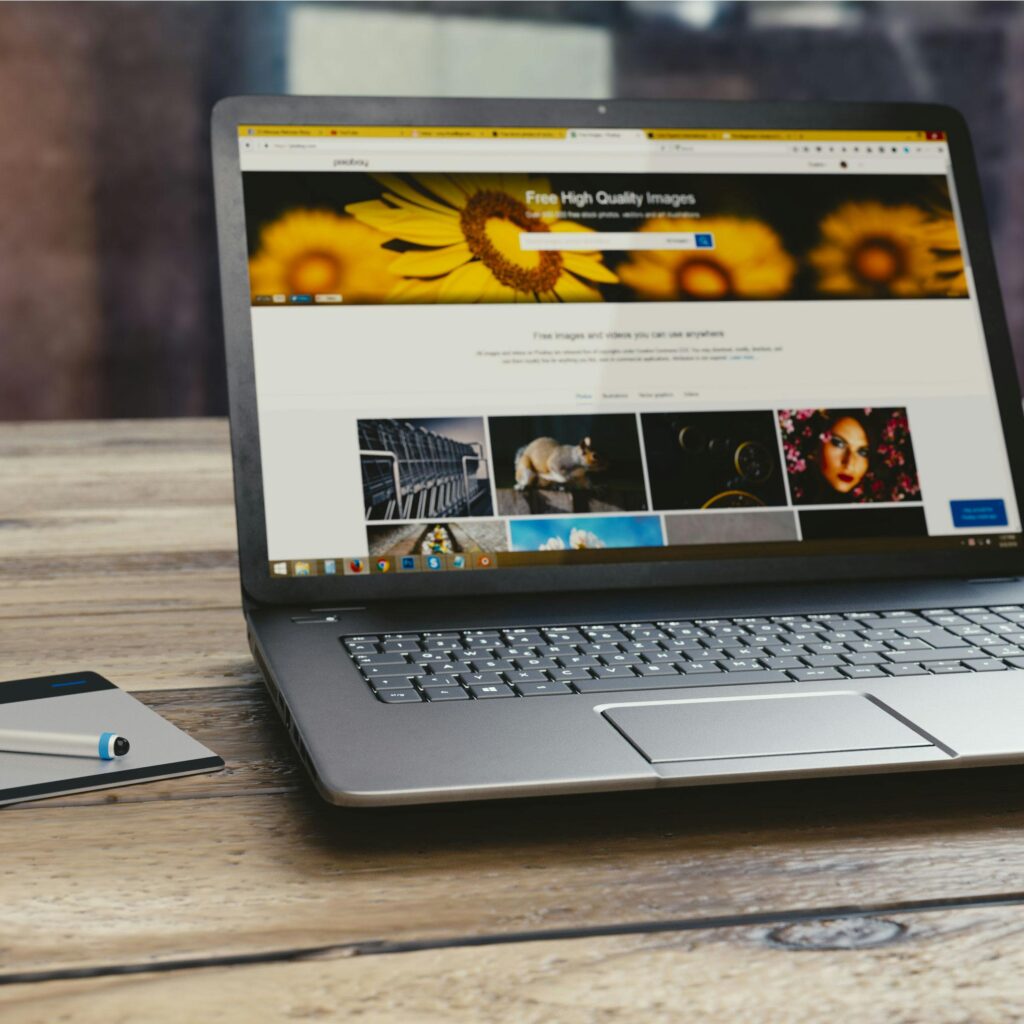 Laptop with open webpage on wooden desk, accompanied by tablet and pen, representing digital work setup.